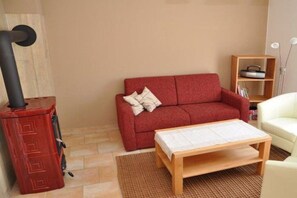A living room with a red sofa, a wooden coffee table, a white armchair, a bookshelf, and a red heater. - Holiday home with 1 bedroom (Kaltenhof (Insel Poel))