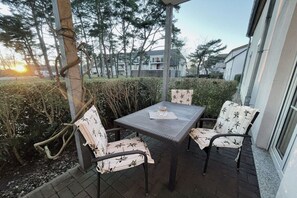 An outdoor patio with a table and two chairs, surrounded by a hedge and trees. - Holiday apartment with 1 bedroom (Dierhagen)