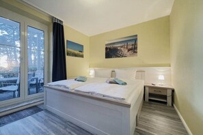 Quarto com cama, mesa de cabeceira, janela com cortinas e vista para o exterior.