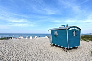 A beachside shack with a sign reading 'Strandkörbe' on wheels, located on a sandy beach with the ocean in the background. - Holiday home in Hohwacht with swimming pool (Hohwacht)