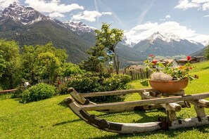 Ländliche Landschaft mit einem hölzernen Boot auf einer Wiese, einem Blumentopf und einem Berg im Hintergrund.