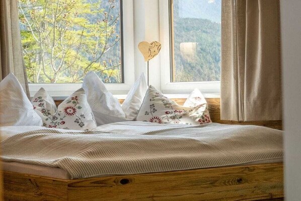 A bed with a wooden frame, white bedding, and decorative pillows with floral patterns. - Stubai farmhouse apartment (Telfes)
