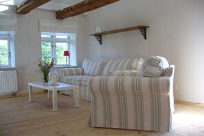 A living room with a striped sofa, a white table, and a window with a view of greenery. - Holiday home in Bobbin with swimming pool (Bobbin)