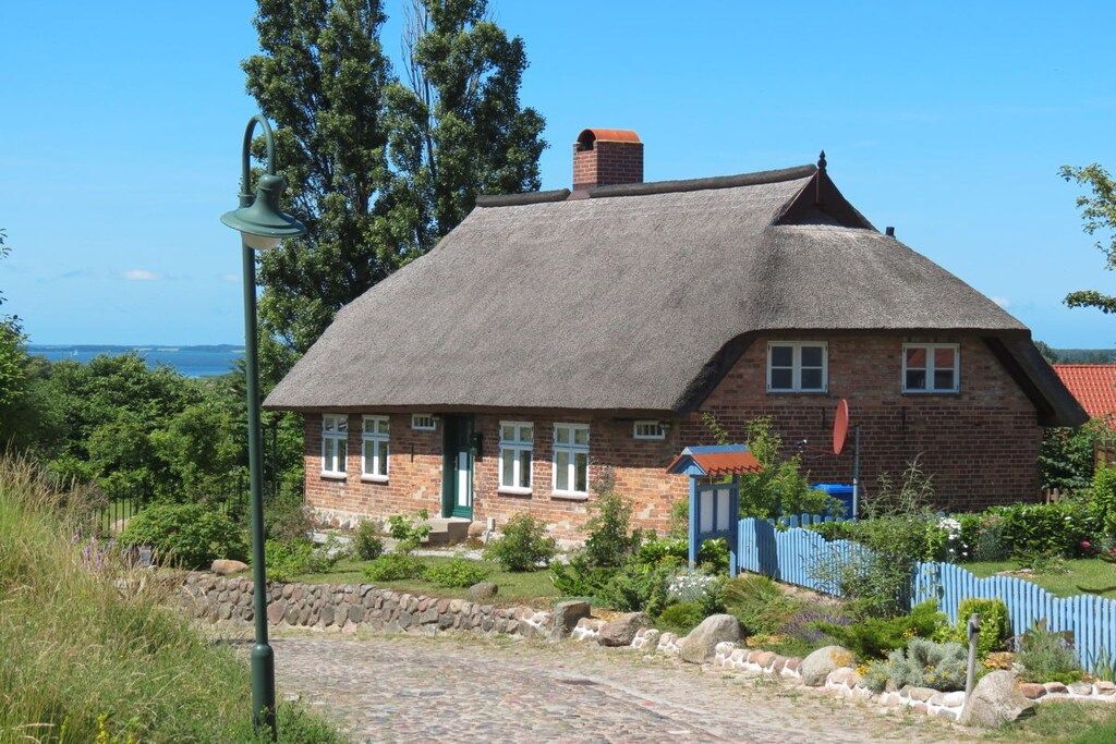 A traditional brick house with a thatched roof, a stone pathway, and a view of the sea.