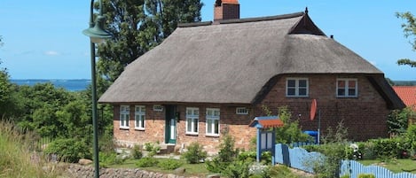 A traditional brick house with a thatched roof, a stone pathway, and a view of the sea.