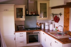 A kitchen with white cabinets, a stove, an oven, and a sink with a dish rack. - Holiday home in Bobbin with swimming pool (Bobbin)