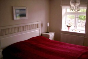 A bedroom with a bed, a nightstand, a lamp, a window with a view of greenery, and a radiator. - Holiday home in Bobbin with swimming pool (Bobbin)