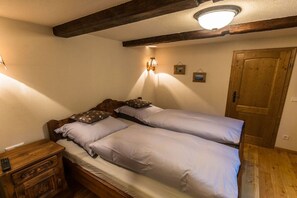 A bedroom with two single beds, a wooden nightstand, a wall-mounted lamp, and a wooden door. - "Small climbing hut" (Bad Schandau OT Krippen)