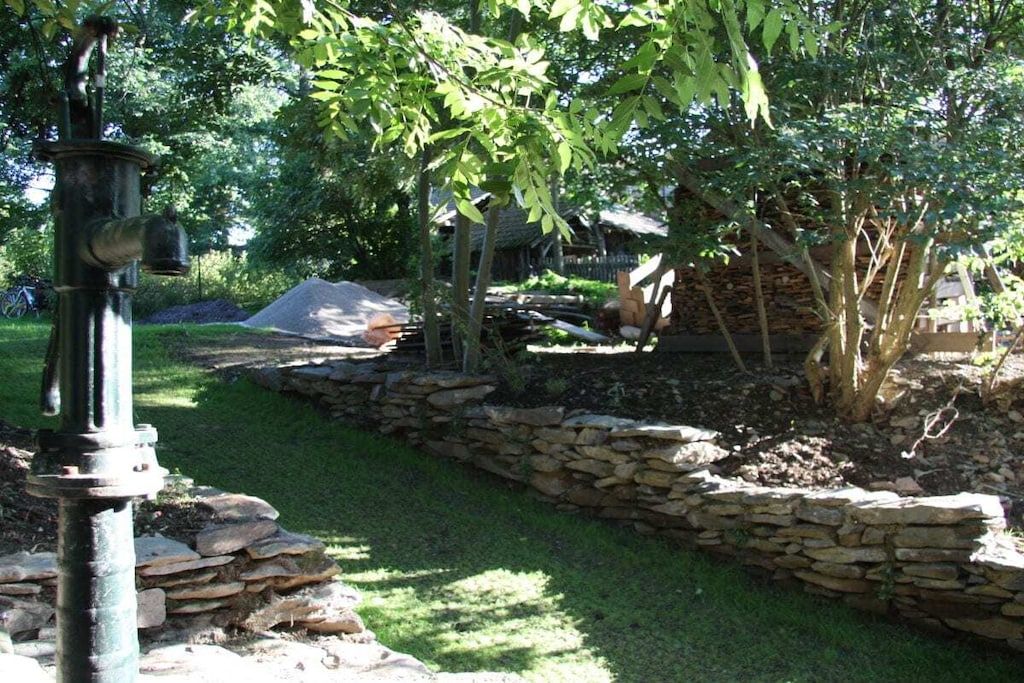 Een tuin met een stenen muur, een metalen constructie en bomen.
