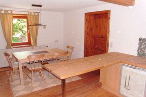 A room with a wooden dining table, chairs, a small kitchenette, and a window with curtains. - Cabin in Drognitz with swimming pool (Drognitz)