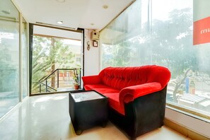 A room with a red sofa, a small black table, and a glass wall offering a view of the outside. - Hotel K L Rooms (Bengaluru)