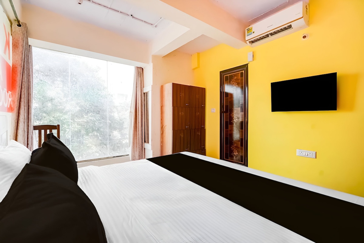 Habitación de hotel con cama, televisor montado en la pared, armario y ventana con cortinas.