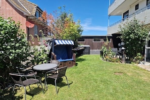 Ein Garten mit einer Terrassentisch- und Stuhlgruppe, einer überdachten Sitzgelegenheit und einem kleinen Garten.