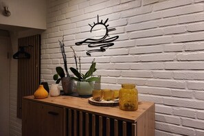 Ein Holzkabinett mit Dekorationselementen vor einer weißen Ziegelwand, ein abstraktes Kunstwerk an der Wand und eine Pendelleuchte.