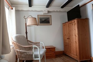 Ein Zimmer mit einem Korbstuhl, einem Holzschrank, einem kleinen Holztisch und einer Stehlampe.