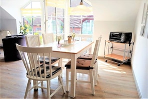 A dining area with a table and chairs, a window with a view, and a kitchen area with a toaster. - Holiday apartment with 3 bedrooms (Schönhagen)