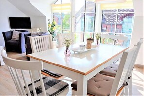 A modern dining area with a white table, white chairs, and a view of the outdoors through large windows. - Holiday apartment with 3 bedrooms (Schönhagen)