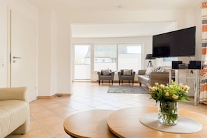A living room with a sofa, a coffee table, a flat-screen TV, and a vase with flowers. - Holiday home Melanie (Scharbeutz)