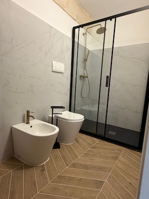 A modern bathroom with a freestanding bathtub, a toilet, and a bidet. The floor has a geometric tile pattern.