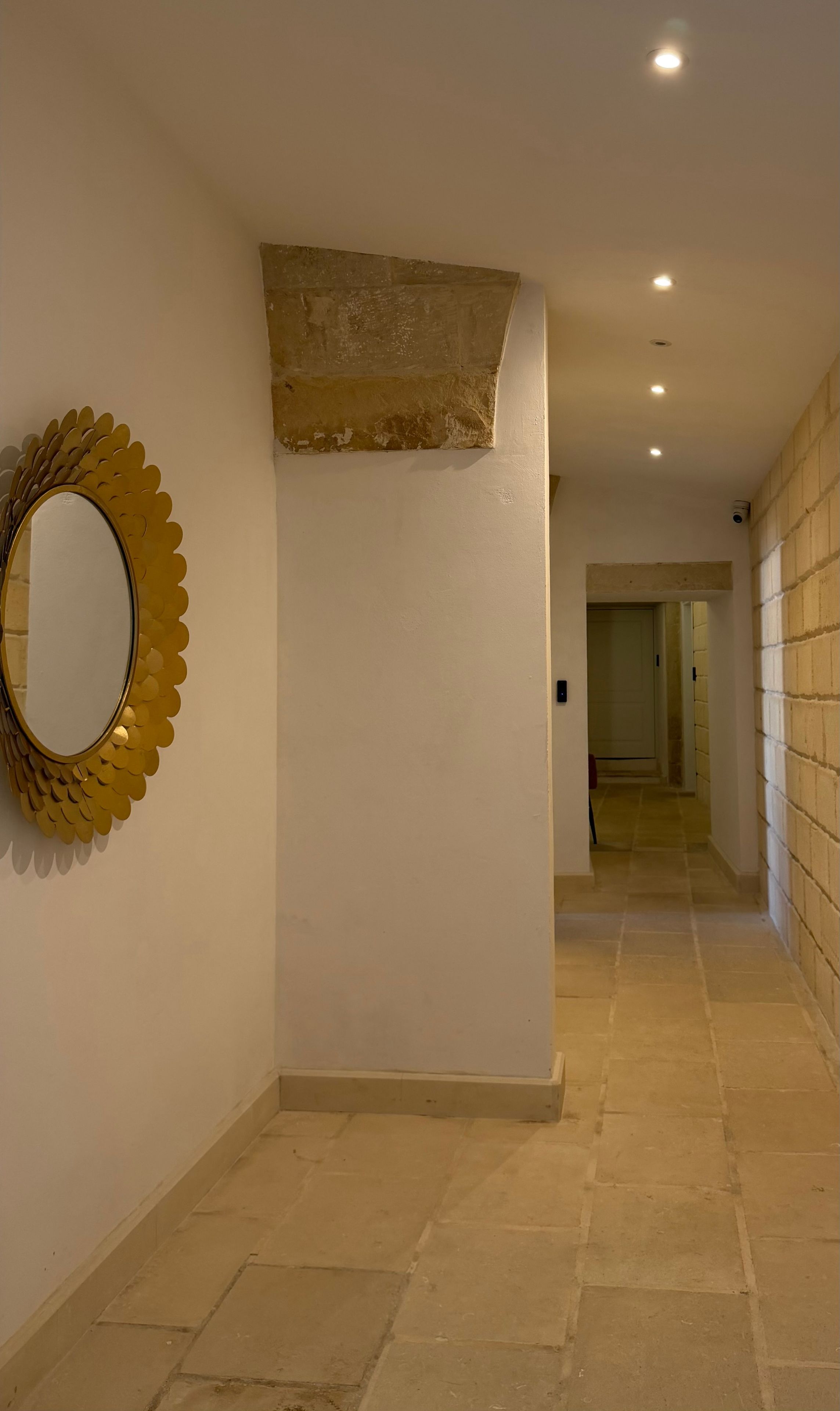 A hallway with a decorative mirror and recessed lighting.