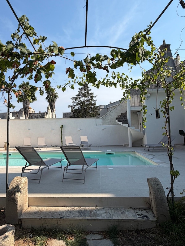 A pool area with lounge chairs, a clear sky, and a building in the background.