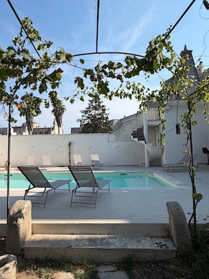 Ein Poolbereich mit Liegestühlen, blauem Himmel und einem Gebäude im Hintergrund.