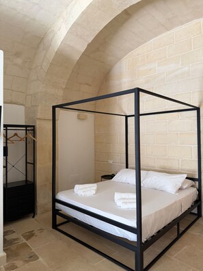 Ein Bett mit Baldachin, ausgestattet mit weißen Leinen, ein Holzschrank mit Kleiderstange und eine Steinwand.