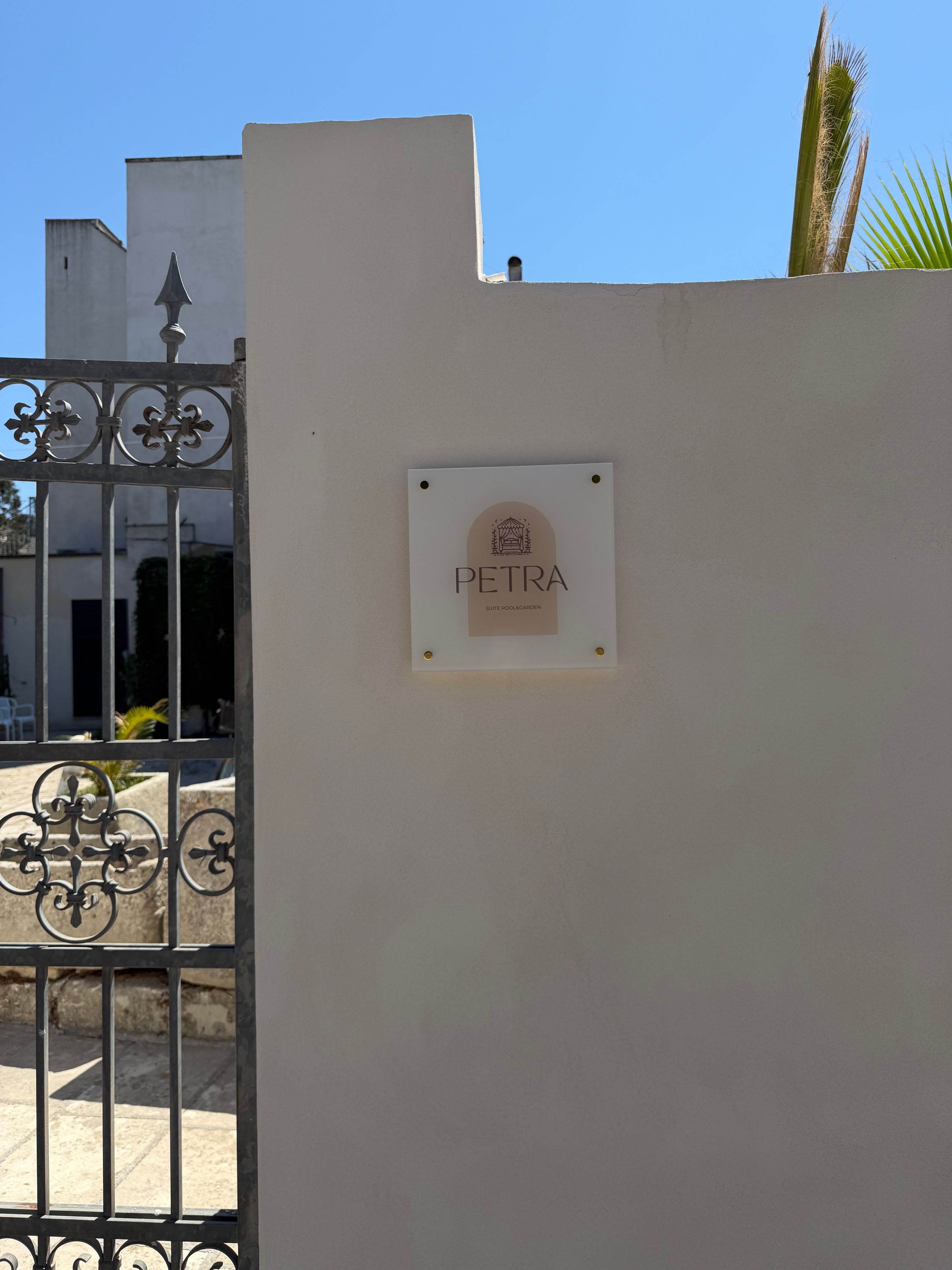 A white wall with a metal gate and a sign that reads 'PETRA SUITE POOLGARDEN.'