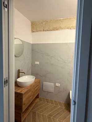 Ein Badezimmer mit weißem Waschbecken, Holz-Waschtisch, Marmorwänden und einem Fischgrätparkettboden.