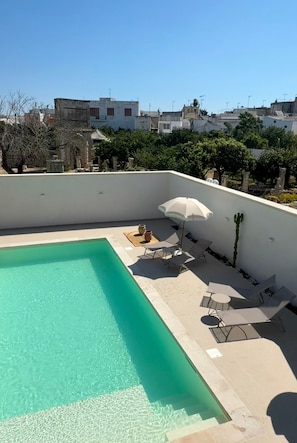 Ein Dachpool mit klarem, blauem Wasser, umgeben von Liegestühlen und einem Sonnenschirm.