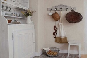 Une cuisine avec des meubles blancs, une porte blanche, un panier suspendu, un panier en osier et une petite table.