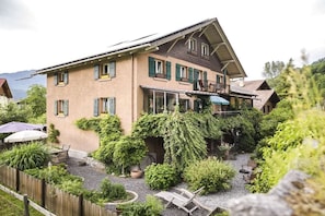 A two-story building with a balcony, surrounded by a garden with various plants and outdoor seating. - Holiday apartment with 2 bedrooms (Wilderswil)