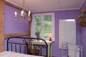 A bedroom with a bed, a desk, a chair, a window with a view of greenery, and a chandelier. - Holiday apartment with 2 bedrooms (Wilderswil)