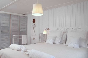 Une chambre à coucher avec un grand lit, du linge de lit blanc, une lampe suspendue et un mur orné d’une inscription décorative.
