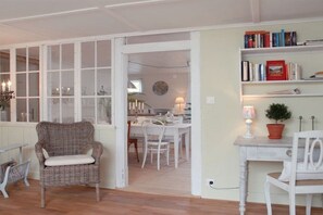 Une pièce avec un fauteuil en osier, un bureau blanc et une bibliothèque.