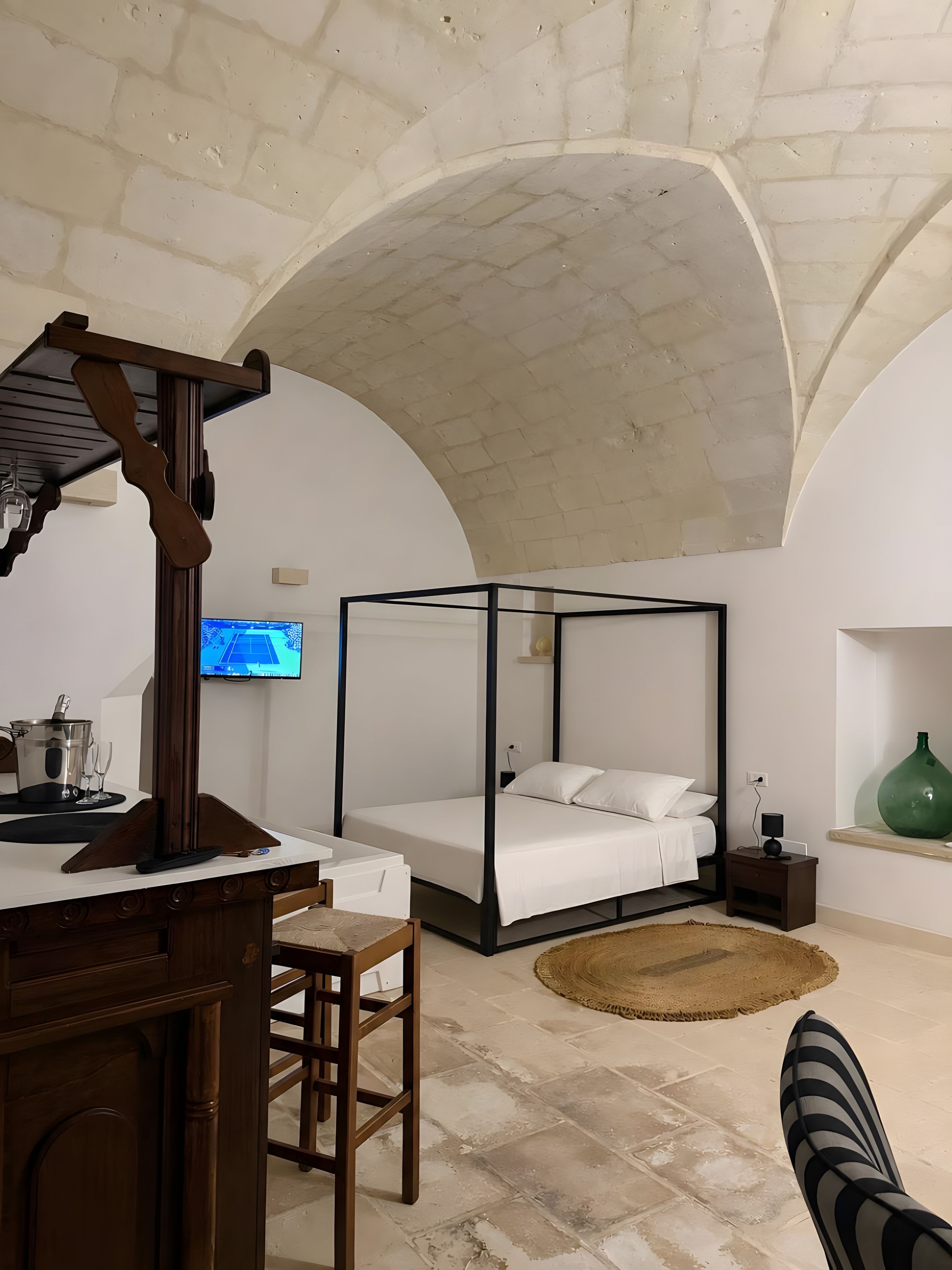 Une chambre à coucher avec un lit à baldaquin, un bureau avec une chaise, une télévision et un vase vert posé sur une étagère.