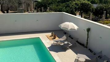 A rooftop swimming pool with a clear blue water, surrounded by lounge chairs and an umbrella.