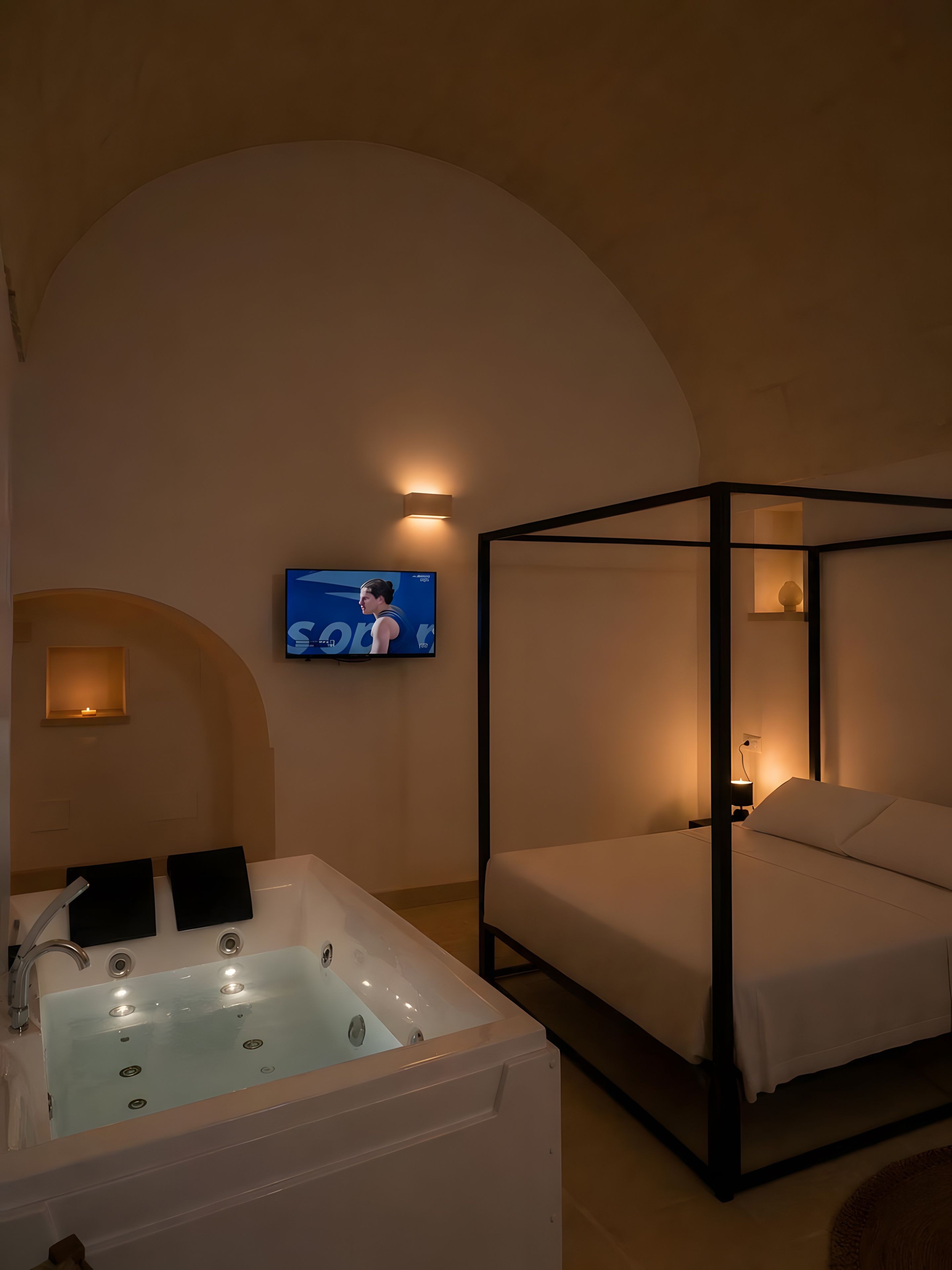 A bedroom with a four-poster bed, a large bathtub, and a television mounted on the wall.