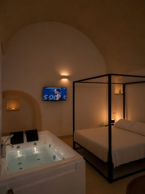 Ein Schlafzimmer mit einem Himmelbett, einer großen Badewanne und einem an der Wand montierten Fernseher.