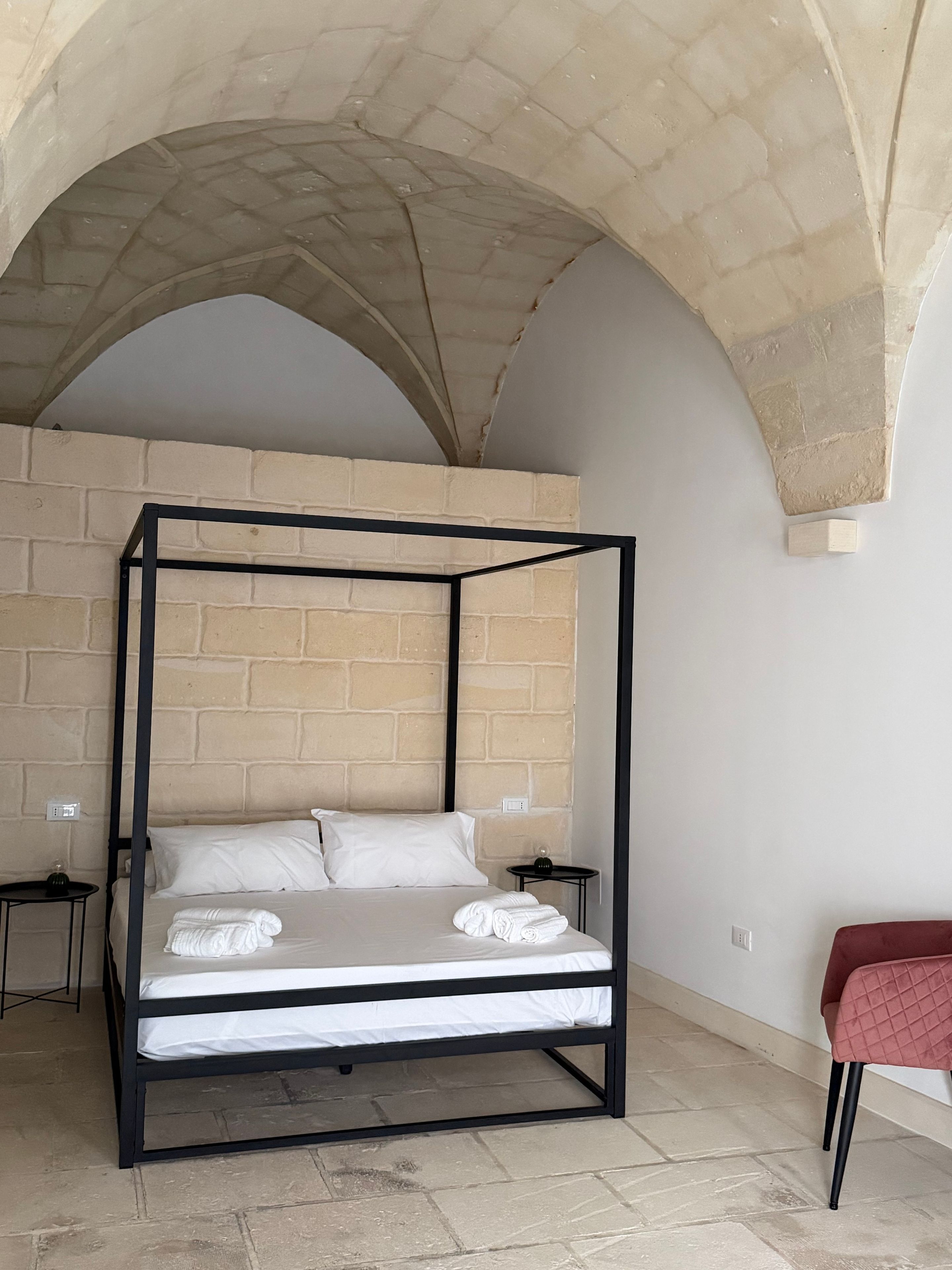 Ein Zimmer mit einem Himmelbett, einem roten Sessel und einer Ziegelwand.
