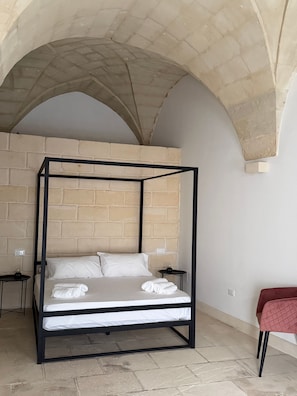 Ein Zimmer mit einem Himmelbett, einem roten Sessel und einer Ziegelwand.