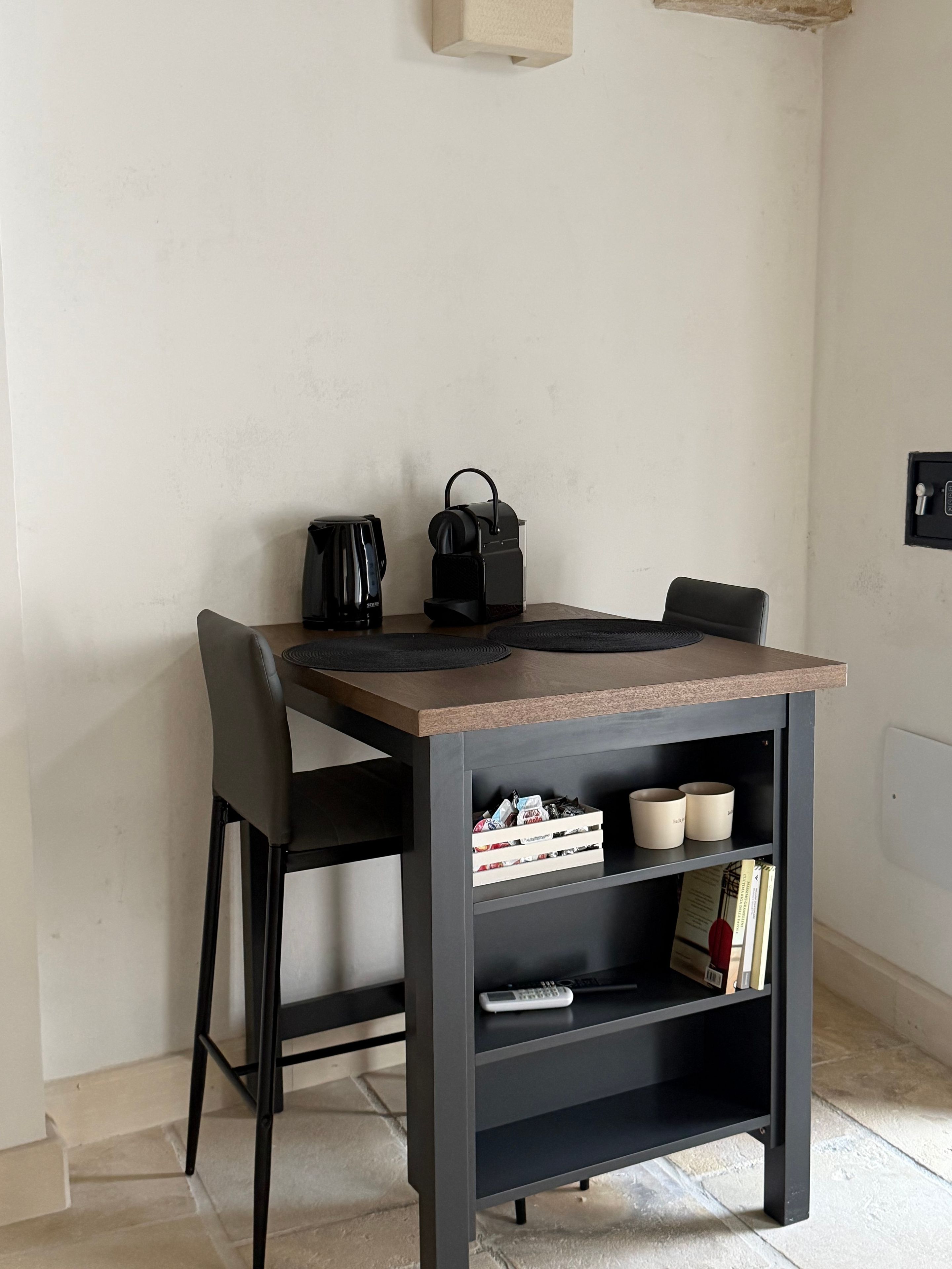 Ein kleiner Essbereich mit Tisch, Stühlen, einer Kaffeemaschine, einem Wasserkocher und einem Bücherregal mit Büchern und Behältern.
