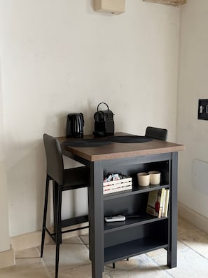 Ein kleiner Essbereich mit Tisch, Stühlen, einer Kaffeemaschine, einem Wasserkocher und einem Bücherregal mit Büchern und Behältern.