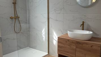 A modern bathroom with a glass-enclosed shower, a wooden vanity with a white sink, and a round mirror.