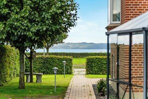 A pathway leading to a conservatory with a view of a body of water and distant hills. - Family home with views over Ebeltoft Bay (Ebeltoft)