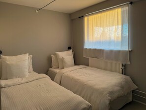 A bedroom with two beds, a radiator, and a window with curtains. - Family home with views over Ebeltoft Bay (Ebeltoft)
