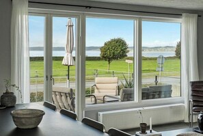 A room with a large window overlooking a grassy area and a body of water. There is a table with chairs and a small plant. - Family home with views over Ebeltoft Bay (Ebeltoft)