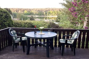 A deck with a round table and four chairs, overlooking a natural landscape with trees and a body of water. - Holiday home with 2 bedrooms (Alt Globsow)
