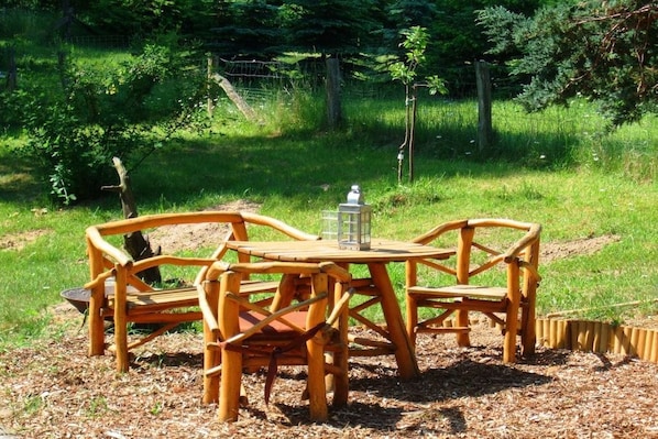 Ein Holz-Garnitur mit Tisch und Stühlen steht auf einer Wiese mit freiem Blick auf die umliegende Natur.