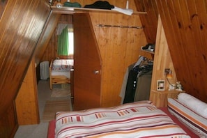 A small, cozy room with a sloped ceiling, a bed with striped bedding, a wooden shelf with personal items, and a door leading to another room. - Holiday home with 2 bedrooms (Alt Globsow)